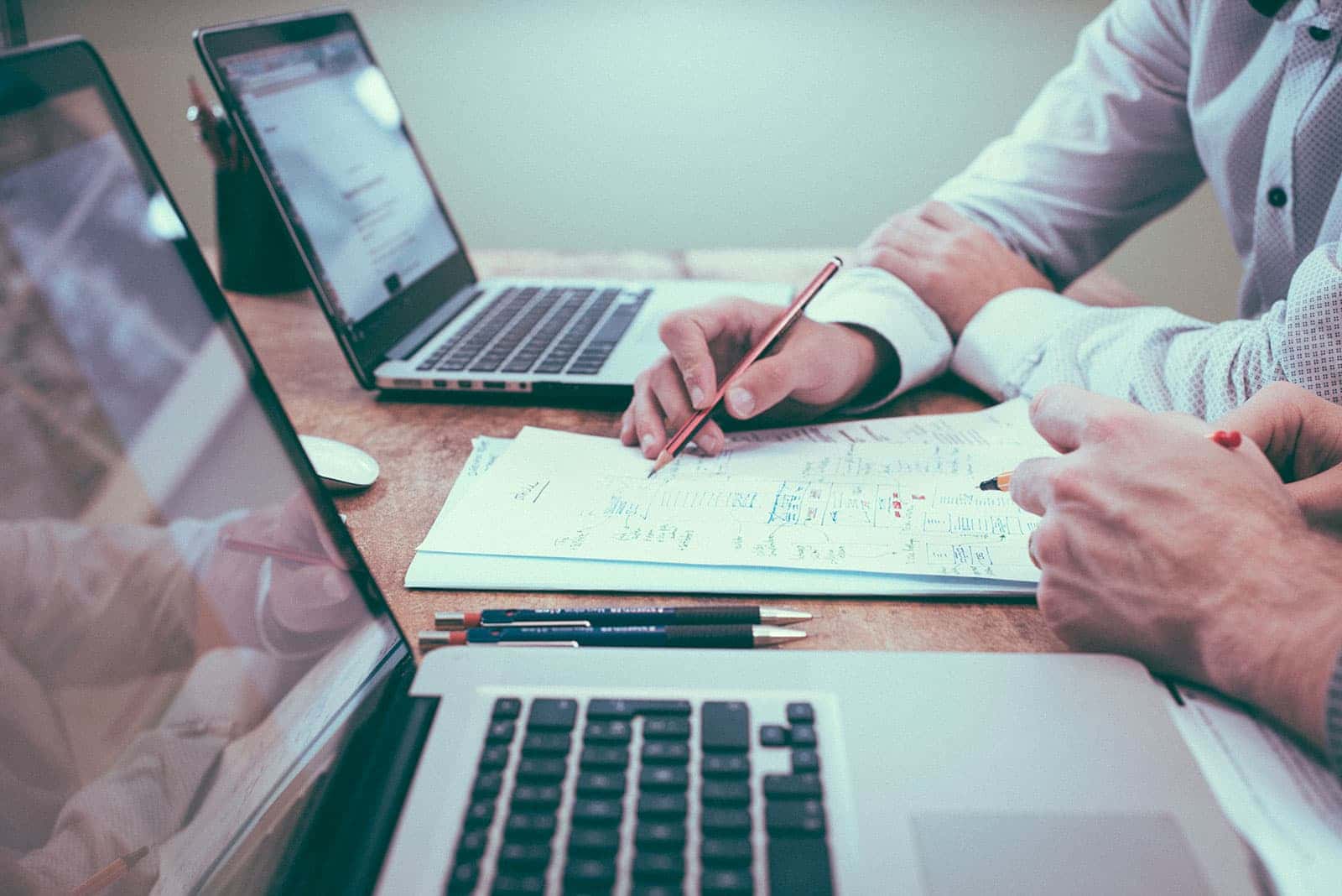 2 Männder arbeiten am Schreibtisch mit Laptop, Papier und Bleistift